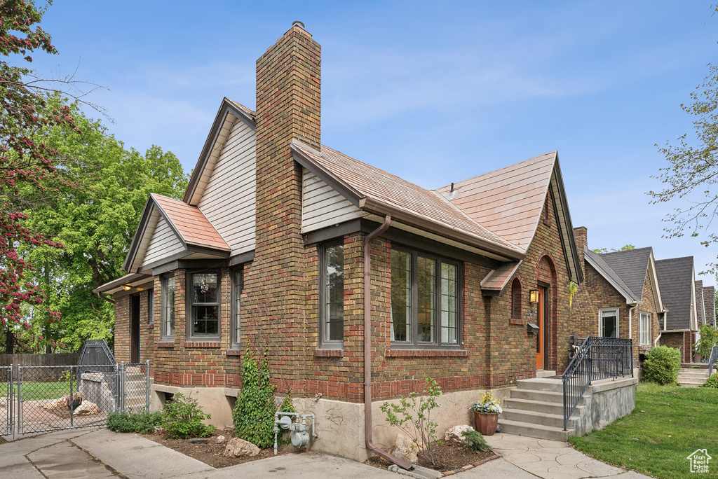 Exterior space with a gate, a chimney, fence, a front yard, and brick siding
