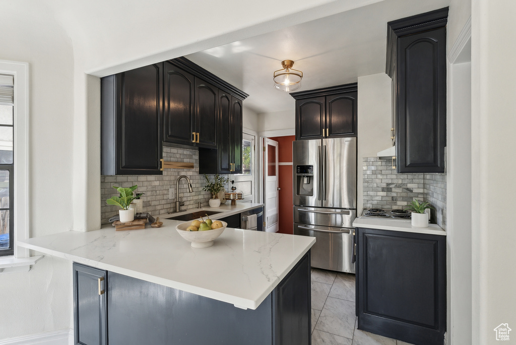 Kitchen featuring a peninsula, a sink, under cabinet range hood, appliances with stainless steel finishes, and tasteful backsplash