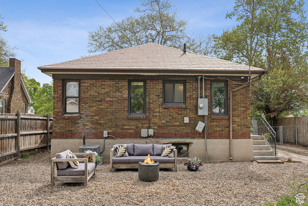 Rear view of property featuring central air condition unit, fence, an outdoor living space with a fire pit, and brick siding