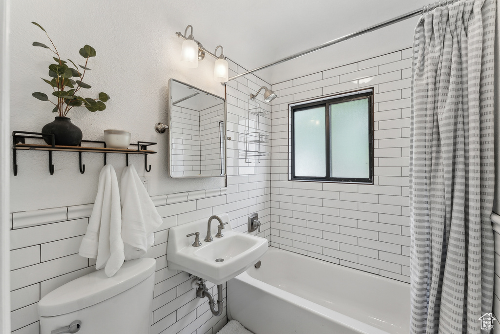 Bathroom with shower / bath combo with shower curtain, toilet, tile walls, and a sink