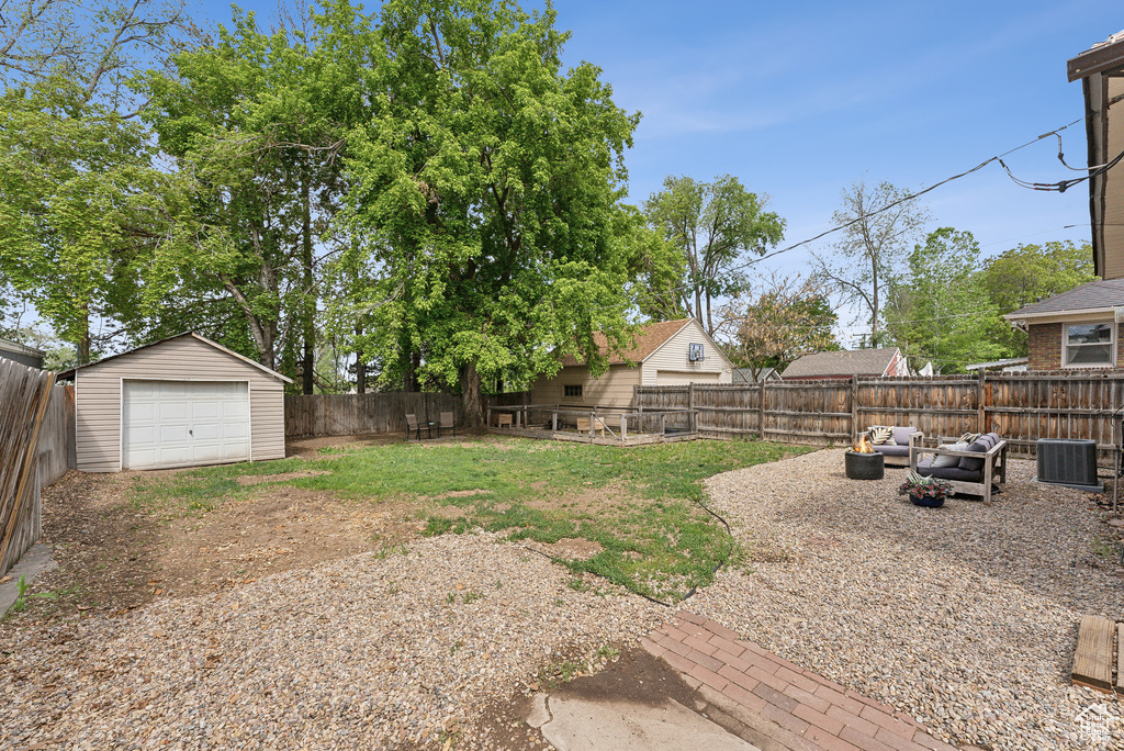 View of yard featuring central AC, a fenced backyard, an outbuilding, driveway, and a detached garage