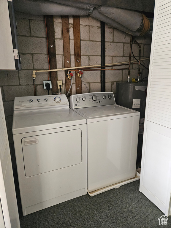 Washroom featuring concrete block wall, washing machine and dryer, dark colored carpet, and water heater