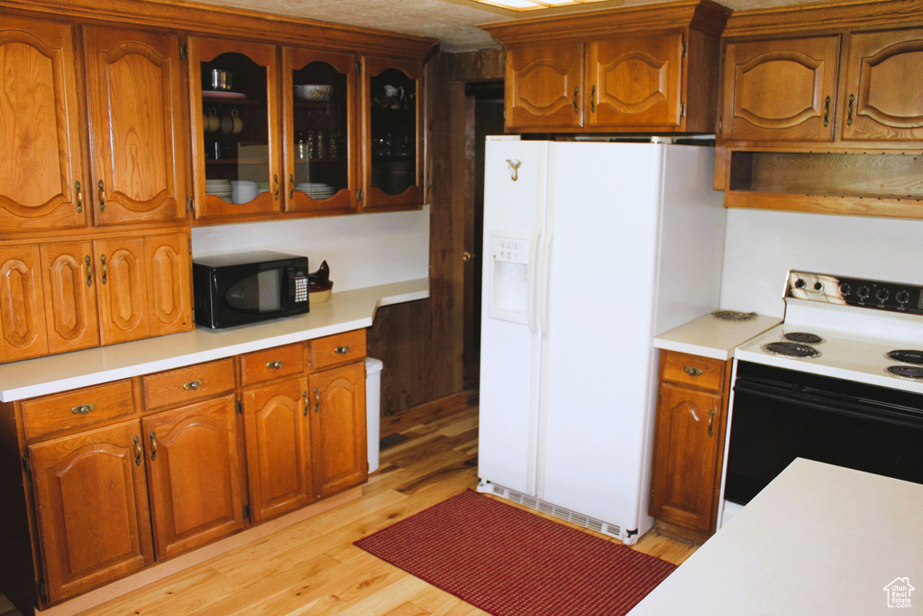 Kitchen featuring range with electric stovetop, black microwave, white refrigerator with ice dispenser, and light countertops