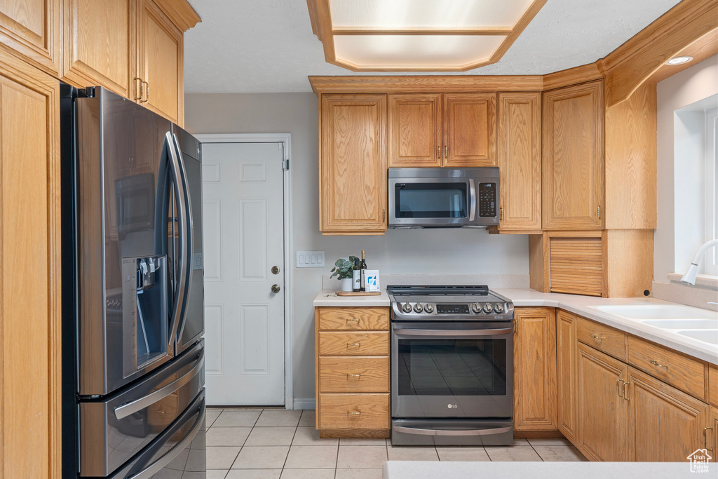 Kitchen with appliances with stainless steel finishes, light tile patterned floors, a sink, and light countertops