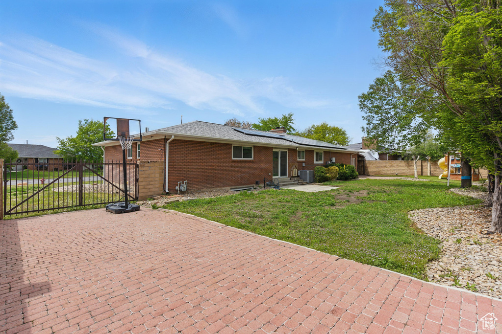 Back of house with entry steps, a gate, brick siding, roof mounted solar panels, and a chimney