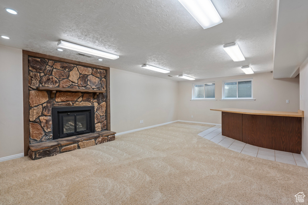 Unfurnished living room featuring light carpet, a textured ceiling, baseboards, a bar, and a stone fireplace