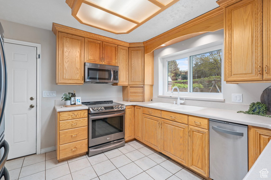 Kitchen featuring stainless steel appliances, a sink, light tile patterned flooring, and light countertops