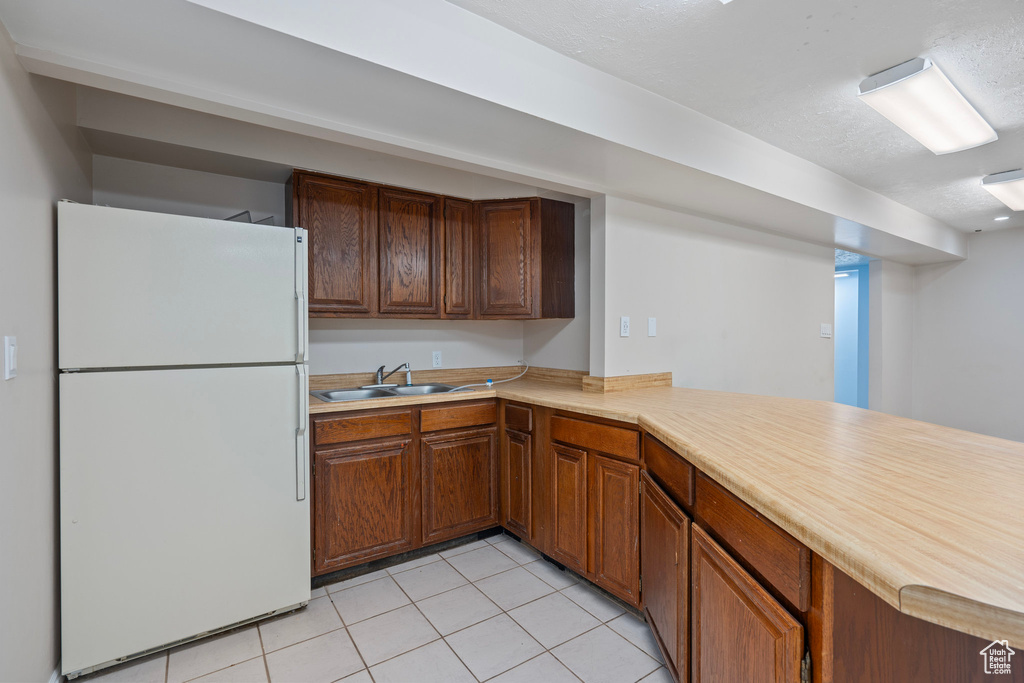 Kitchen featuring freestanding refrigerator, a sink, light tile patterned floors, light countertops, and a textured ceiling