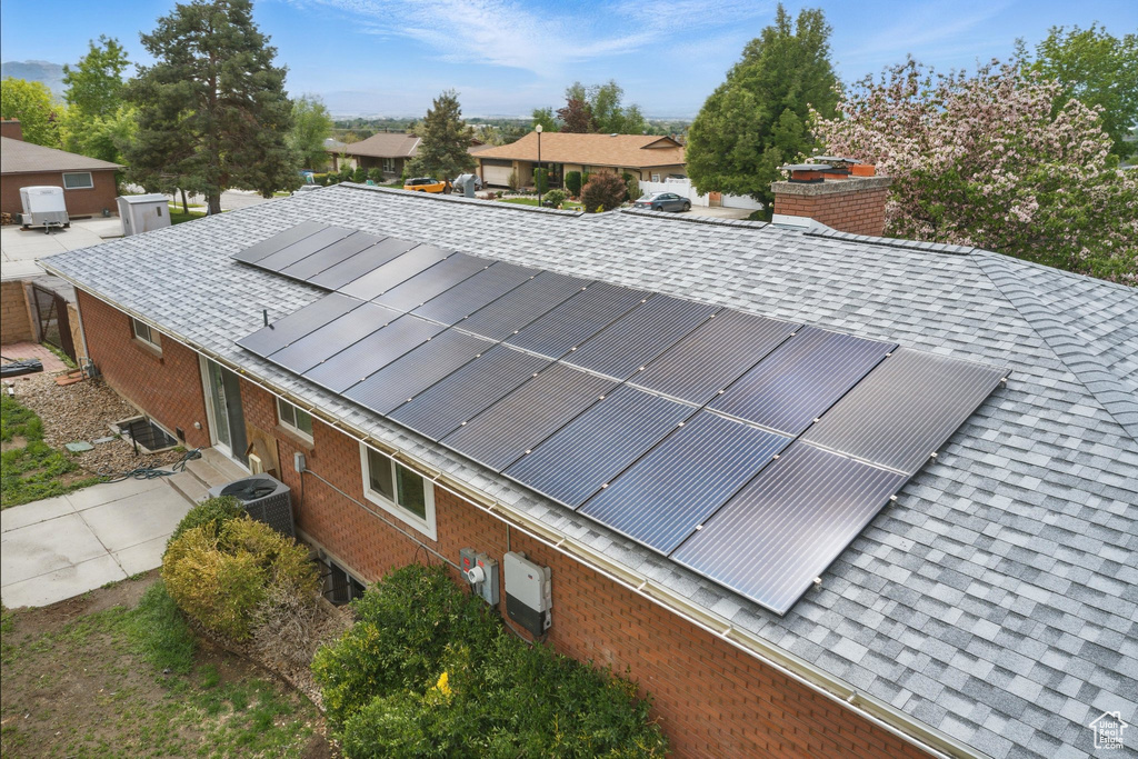 Exterior view of roof with shingles, brick siding, cooling unit, and a residential view