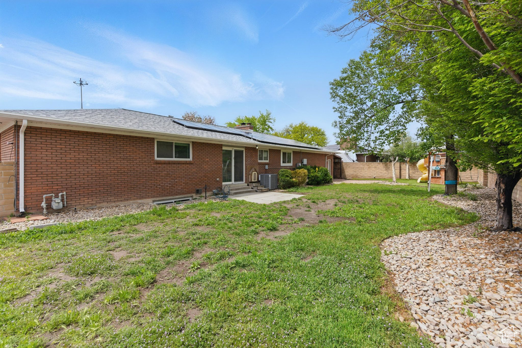 Rear view of property with entry steps, central AC, brick siding, a lawn, and solar panels