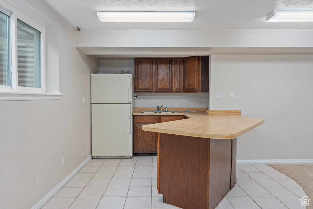 Kitchen with freestanding refrigerator, a peninsula, light countertops, a sink, and light tile patterned flooring