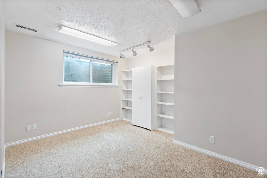 Unfurnished bedroom with carpet flooring, a textured ceiling, baseboards, and track lighting