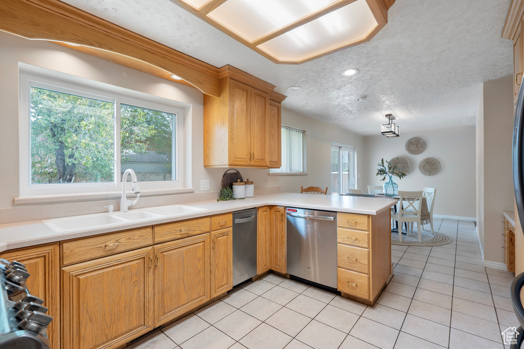 Kitchen with stainless steel dishwasher, a sink, a peninsula, light tile patterned flooring, and light countertops