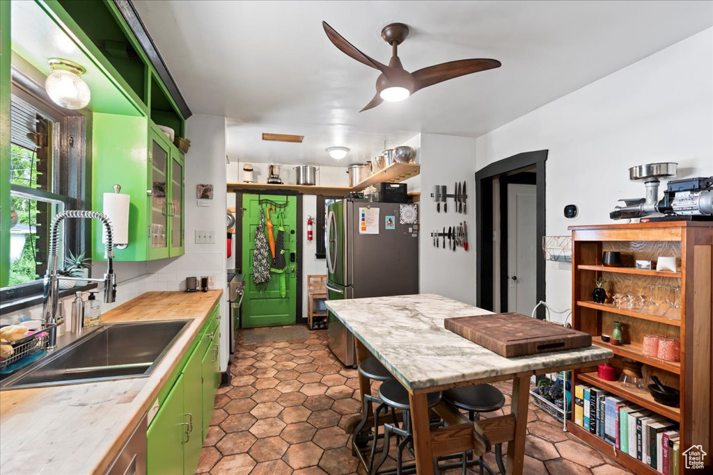 Kitchen with green cabinets, freestanding refrigerator, a ceiling fan, and a sink