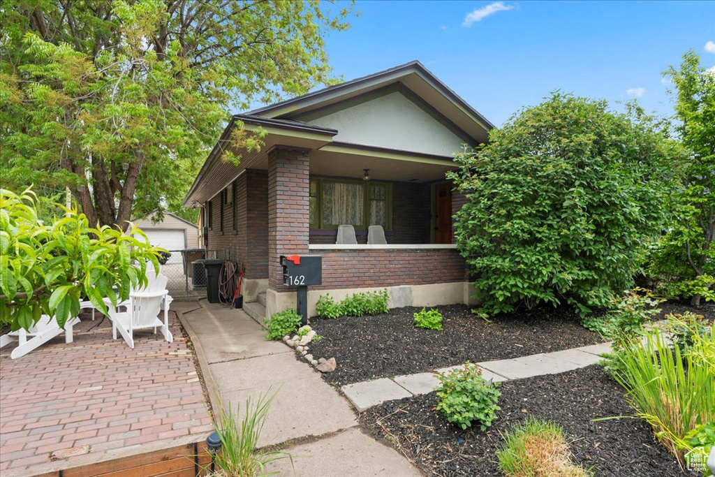 View of front of house with stucco siding, an outdoor structure, a porch, brick siding, and a detached garage
