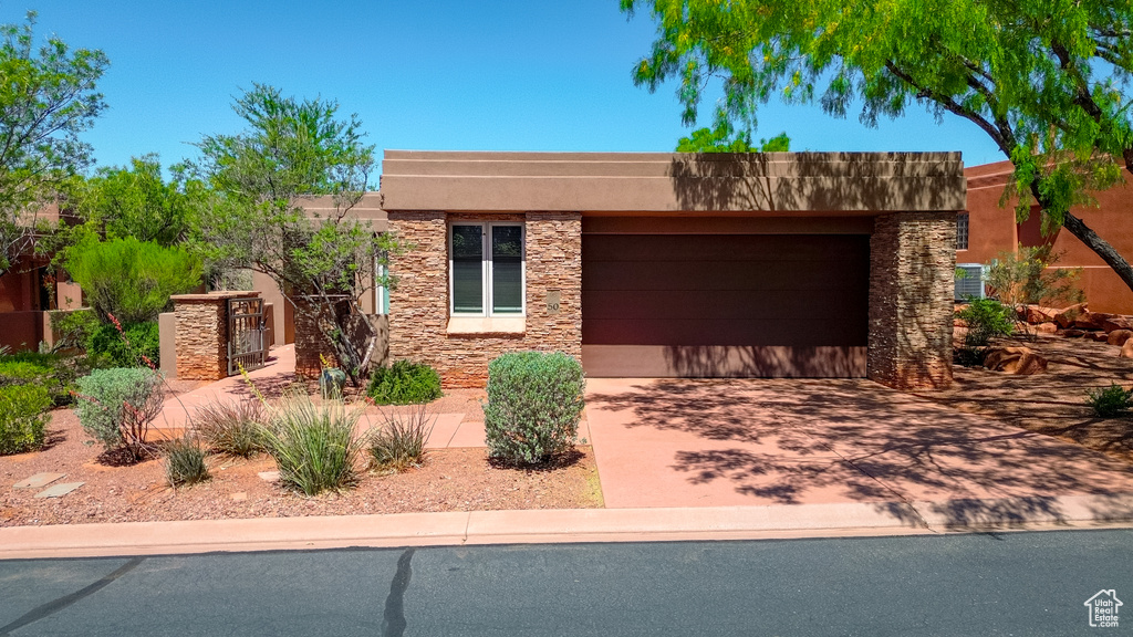Pueblo-style home with concrete driveway, stucco siding, an attached garage, and stone siding