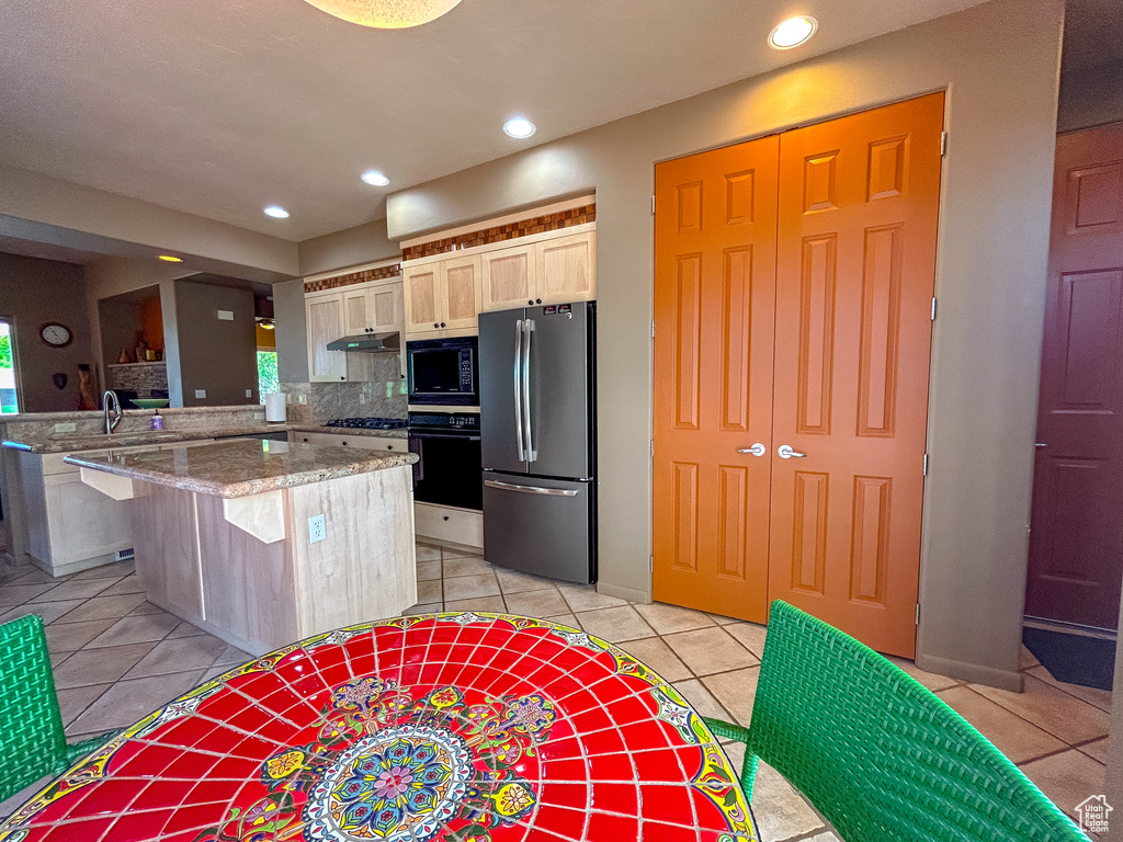 Kitchen featuring a sink, a peninsula, black appliances, under cabinet range hood, and light tile patterned floors
