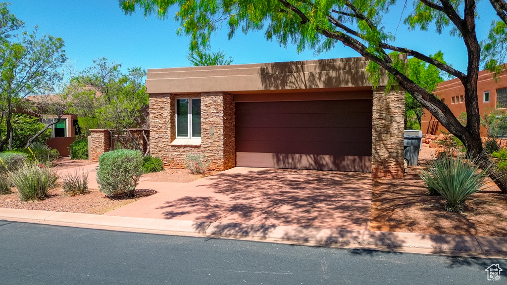 View of front facade featuring stone siding, stucco siding, a garage, and driveway