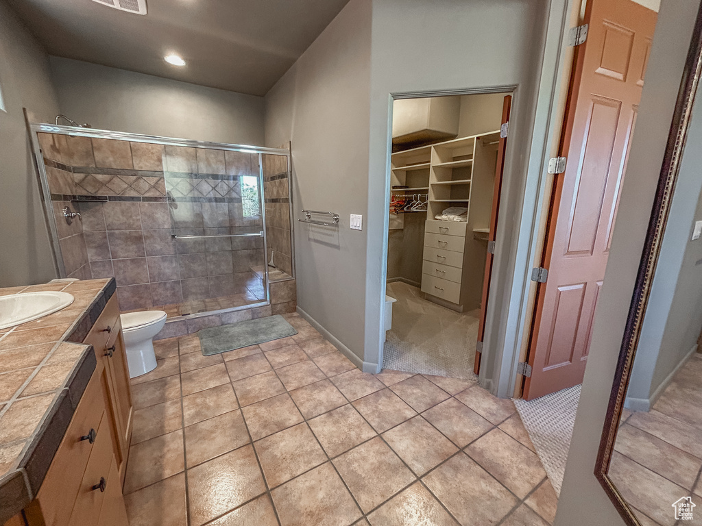 Full bathroom featuring toilet, vanity, tile patterned floors, a stall shower, and a walk in closet