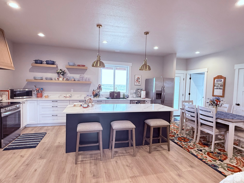 Kitchen featuring appliances with stainless steel finishes, a center island, light wood-style floors, light stone countertops, and recessed lighting