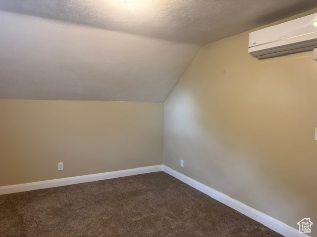 Additional living space featuring a wall mounted air conditioner, lofted ceiling, carpet floors, baseboards, and a textured ceiling