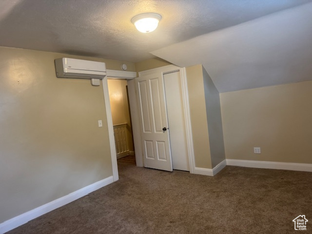 Bonus room featuring a wall unit AC, carpet flooring, baseboards, a textured ceiling, and vaulted ceiling