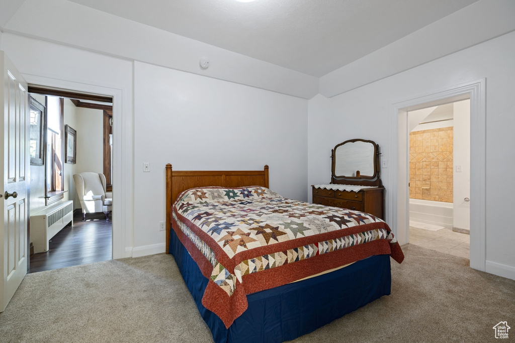 Bedroom with radiator heating unit, carpet flooring, baseboards, and ensuite bathroom