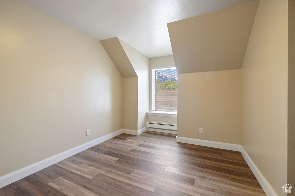 Additional living space featuring a baseboard heating unit, wood finished floors, vaulted ceiling, and baseboards