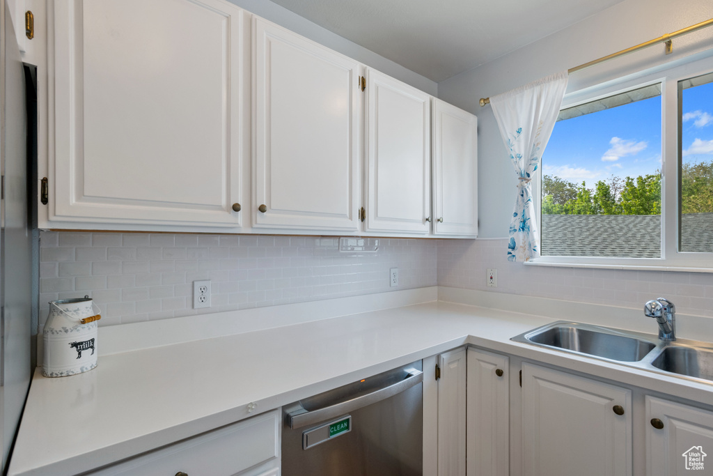 Kitchen with dishwasher, a sink, backsplash, and white cabinets