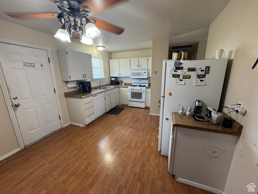 Kitchen with white appliances, a sink, a ceiling fan, wood finished floors, and white cabinetry