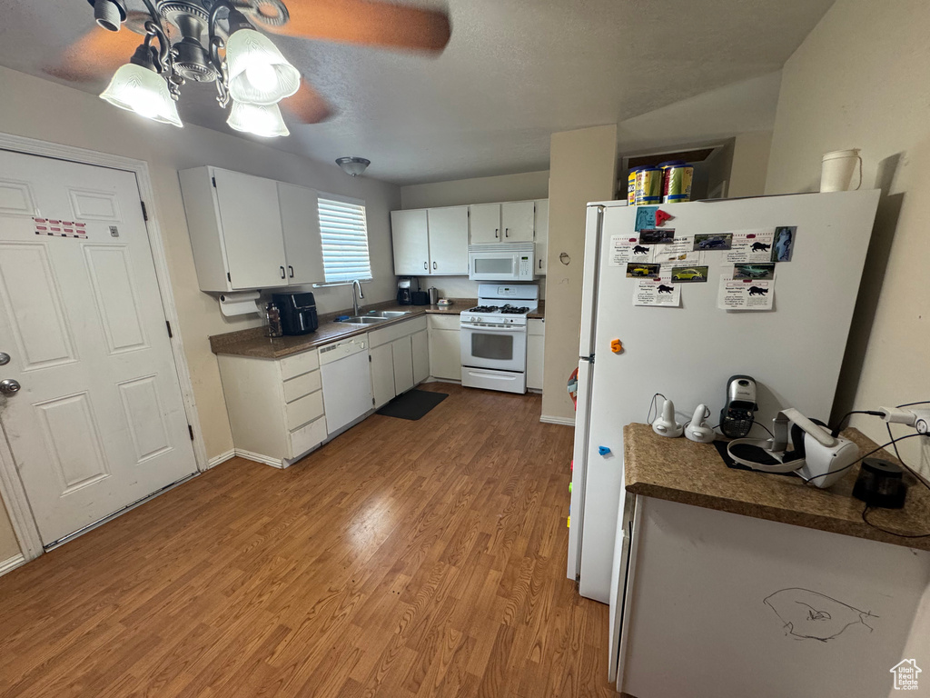 Kitchen featuring white appliances, a sink, wood finished floors, white cabinetry, and dark countertops