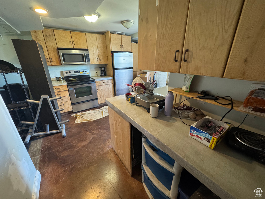 Kitchen featuring appliances with stainless steel finishes, light countertops, unfinished concrete flooring, and light brown cabinetry