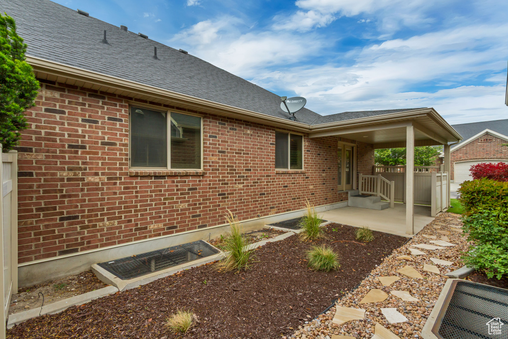 Rear view of property with brick siding, roof with shingles, and a patio area