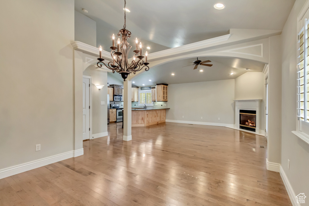 Unfurnished living room featuring a ceiling fan, arched walkways, a glass covered fireplace, light wood-type flooring, and recessed lighting