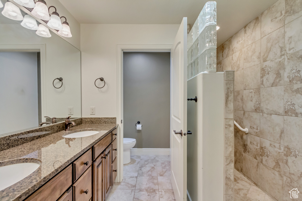 Full bath with toilet, a walk in shower, double vanity, and marble finish flooring