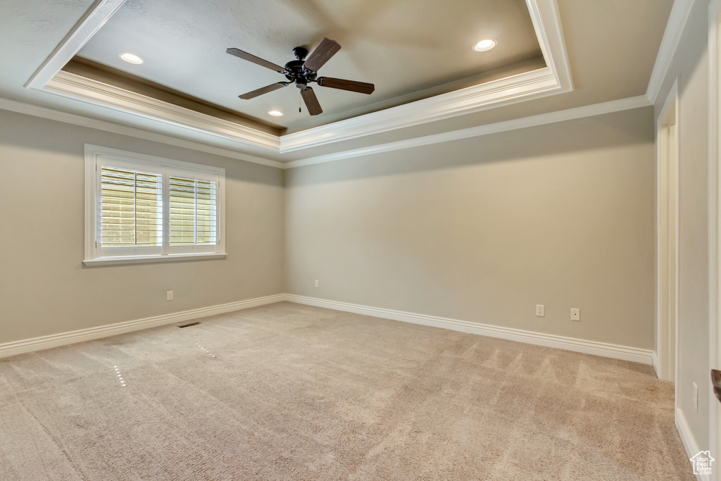 Empty room featuring a raised ceiling, crown molding, light colored carpet, ceiling fan, and recessed lighting
