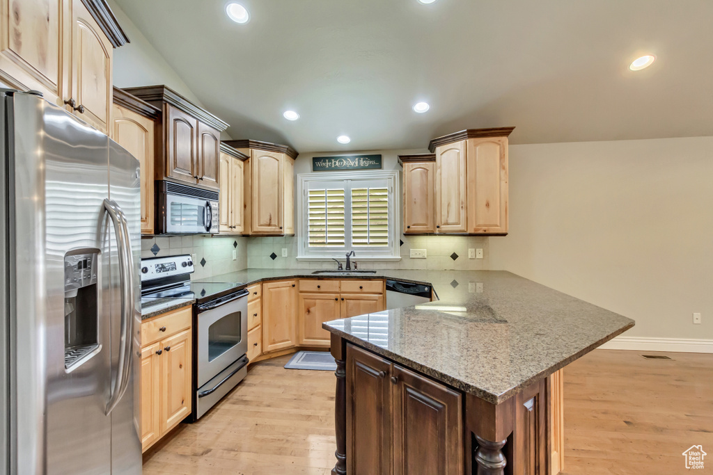 Kitchen with appliances with stainless steel finishes, a peninsula, light brown cabinetry, light wood-style flooring, and recessed lighting