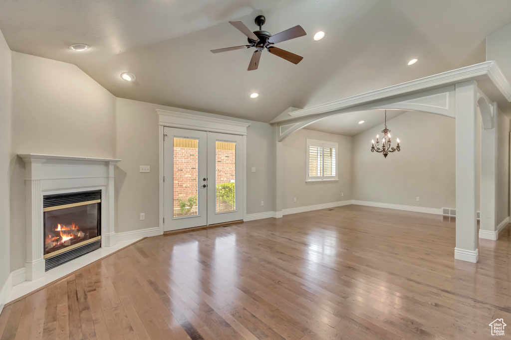 Unfurnished living room featuring vaulted ceiling, a glass covered fireplace, wood finished floors, ceiling fan, and french doors