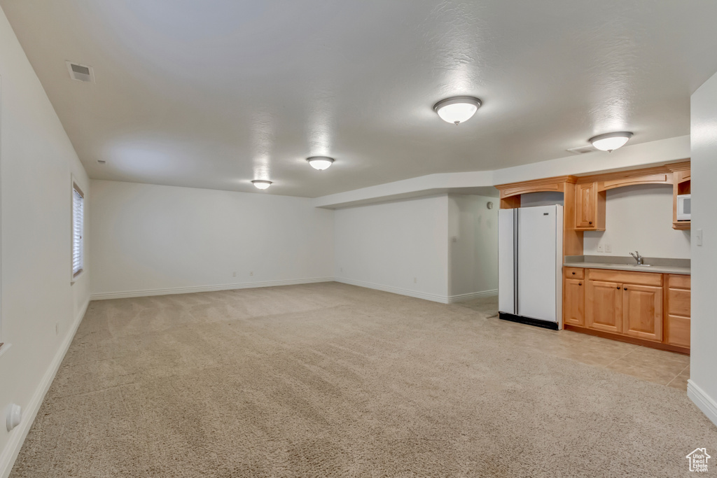 Below grade area with freestanding refrigerator, a sink, light colored carpet, and baseboards