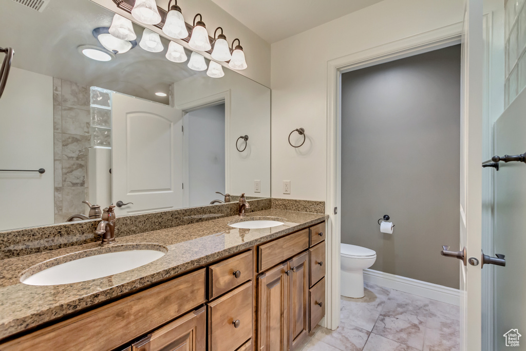 Full bath featuring marble look tiles, toilet, double vanity, and baseboards