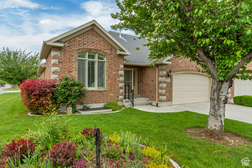View of front of home with an attached garage, driveway, brick siding, a front lawn, and roof with shingles