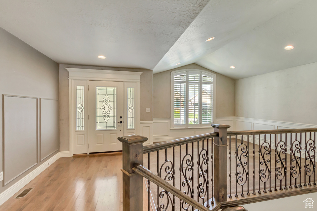 Entryway featuring vaulted ceiling, a decorative wall, a wainscoted wall, and wood finished floors