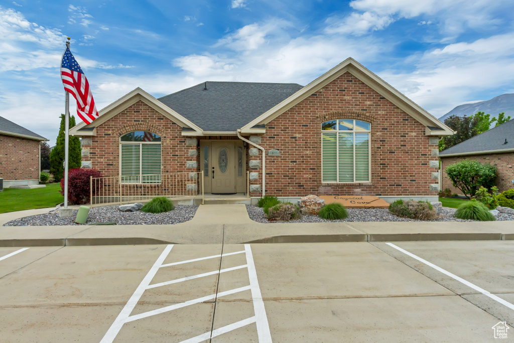 View of front of house with brick siding, uncovered parking, and roof with shingles