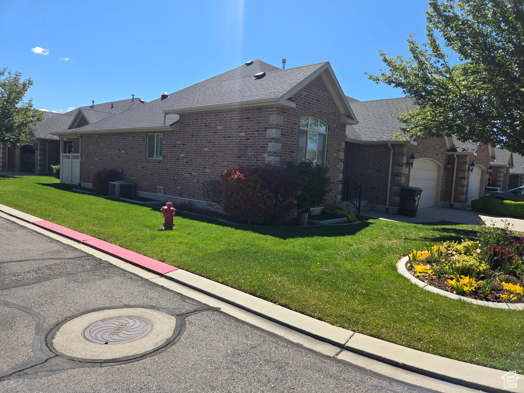 View of side of home with brick siding, a lawn, an attached garage, a shingled roof, and central AC unit