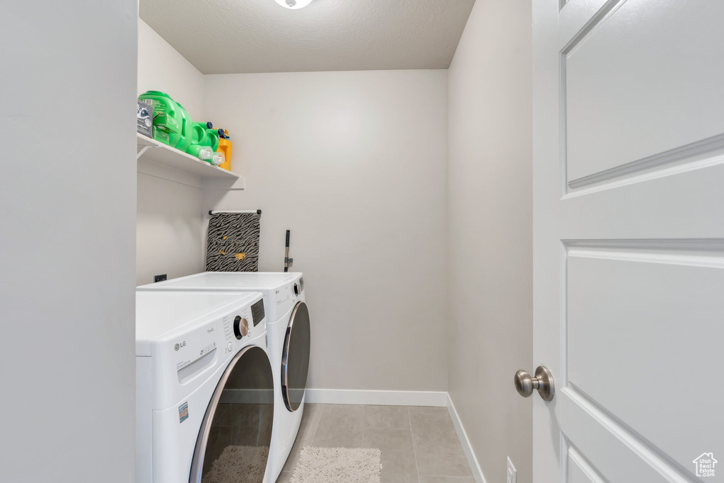Clothes washing area featuring washing machine and dryer, light tile patterned floors, and baseboards