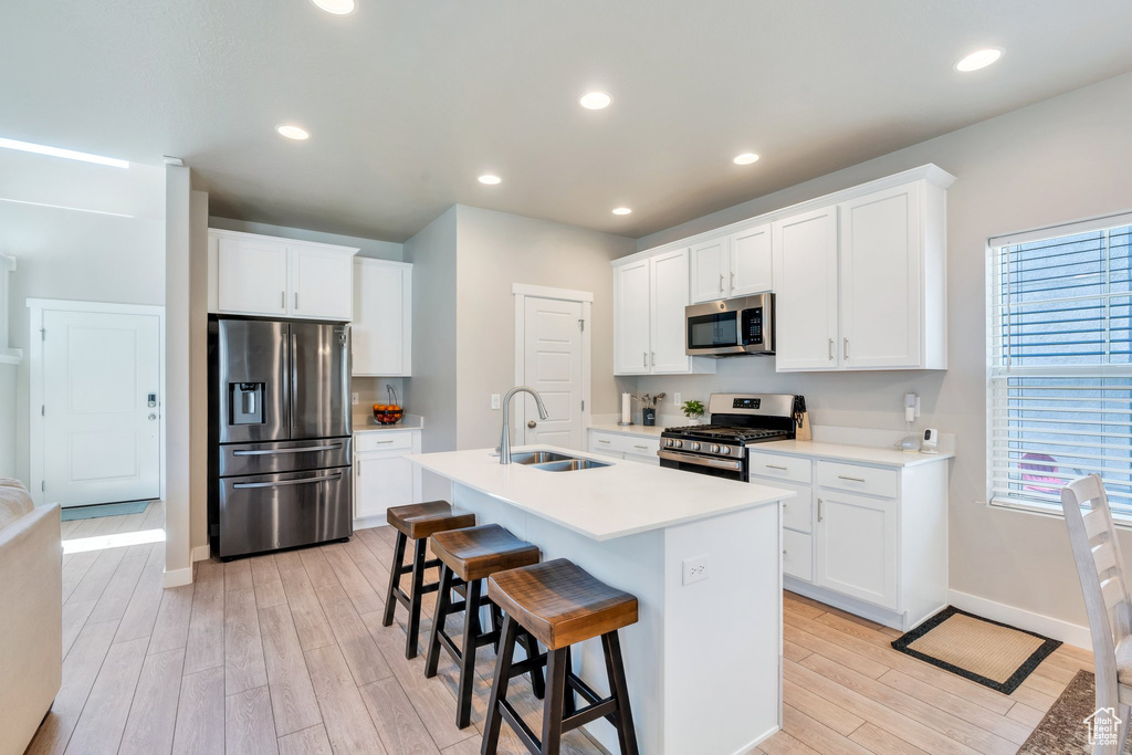 Kitchen with stainless steel appliances, a sink, light wood-style floors, baseboards, and a breakfast bar