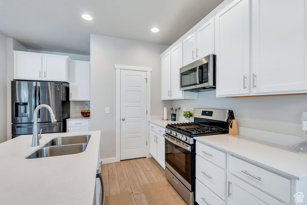 Kitchen with stainless steel appliances, a sink, light wood finished floors, white cabinetry, and light countertops