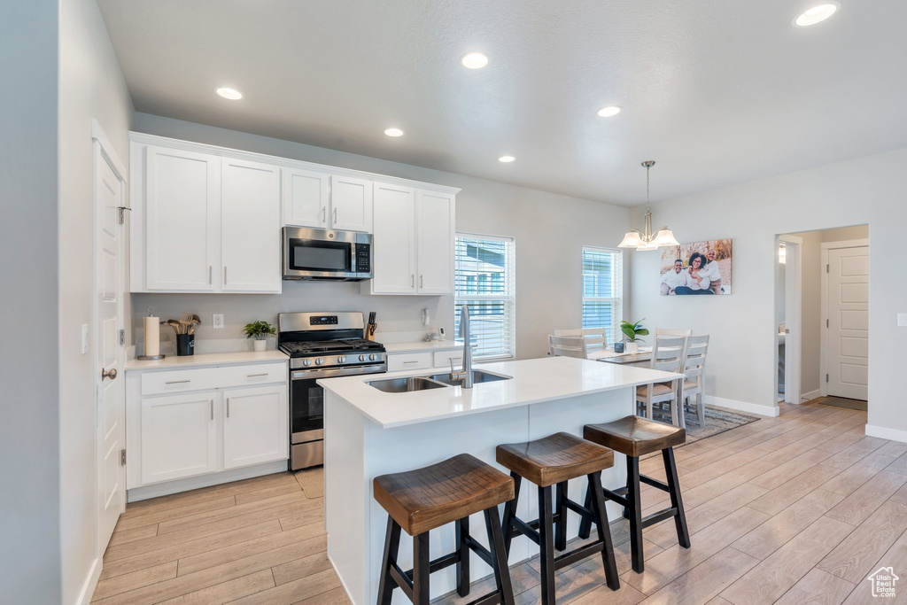 Kitchen with appliances with stainless steel finishes, a sink, light wood-type flooring, white cabinetry, and a center island with sink