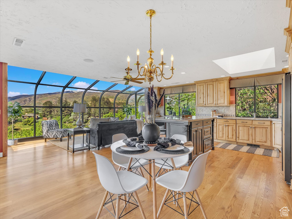 Dining area with light wood-style floors, a skylight, and a chandelier