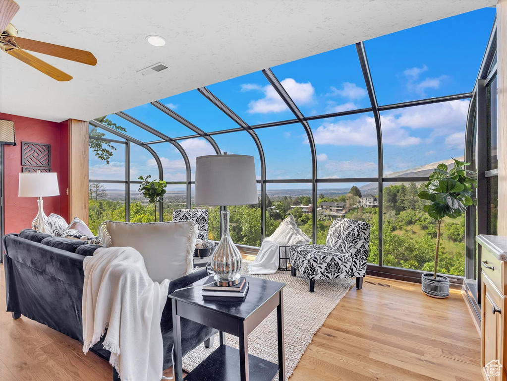 Living area with a sunroom, a ceiling fan, plenty of natural light, wood finished floors, and expansive windows